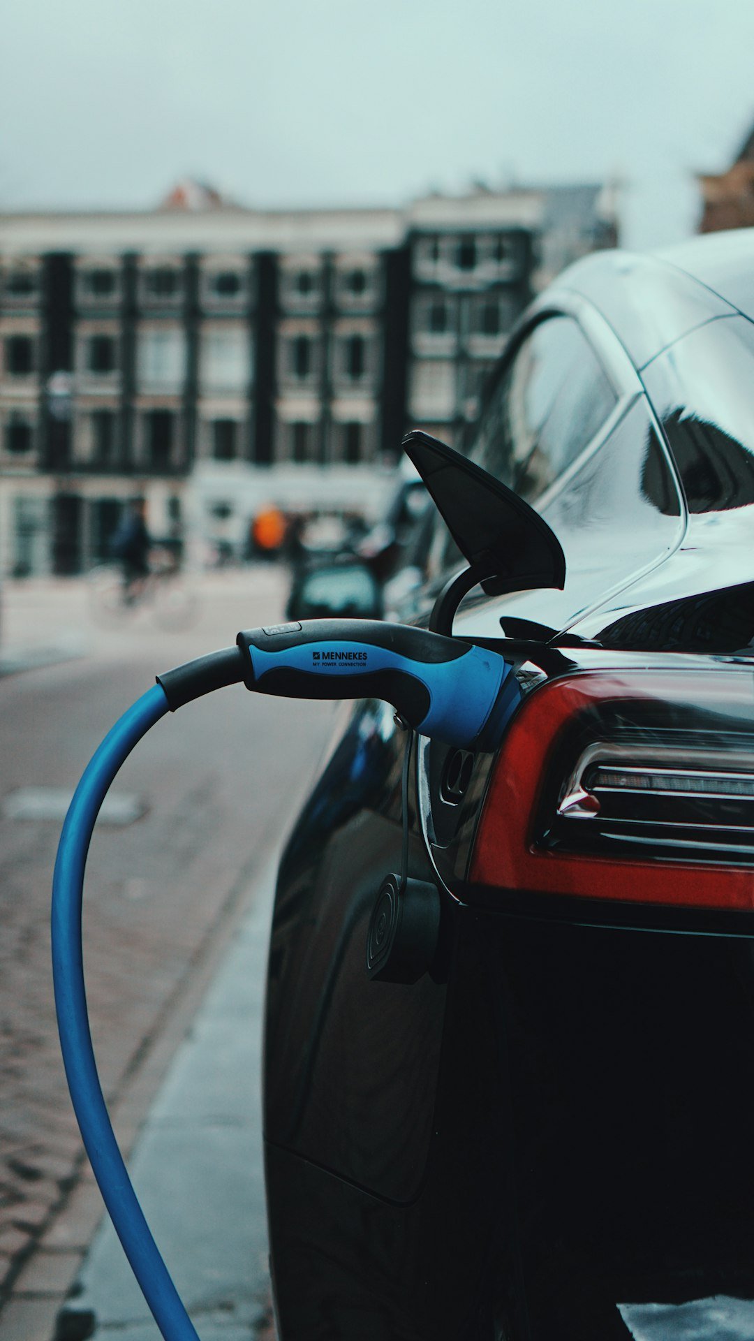 Electric car charging on a city street with a blue cable
